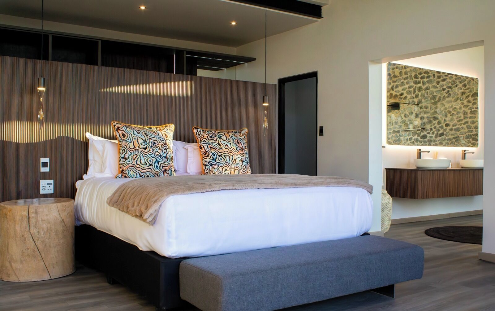 A modern bedroom with a large bed, a wooden headboard, and a stone-patterned wall.