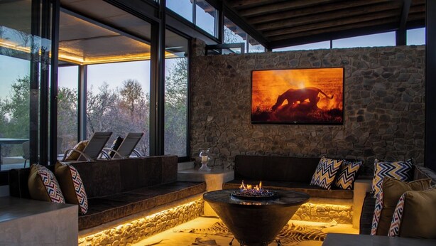 A modern outdoor seating area with a stone wall, a fire pit, and a large framed picture of a sunset.
