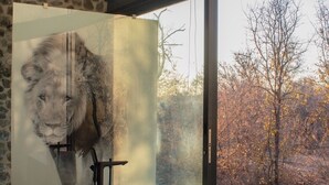 A modern bathroom with a large window, a stone wall, and a large painting of a lion.