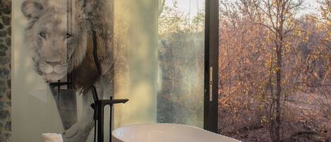 Ein modernes Badezimmer mit großem Fenster, einer Steinwand und einem großen Gemälde eines Löwen.
