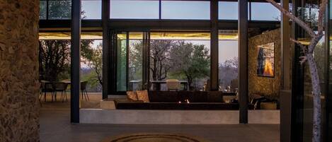 A modern interior with large windows, a stone wall, and a seating area with a fire feature.