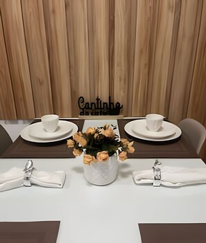 A dining table set with white plates, bowls, and a centerpiece of dried flowers in a white vase. - Apartamento de luxo com varanda 2 Qtos (Cabedelo)