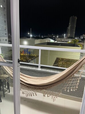 A balcony with a hammock, a view of the cityscape at night, and a staircase leading to an upper level. - Apartamento de luxo com varanda 2 Qtos (Cabedelo)