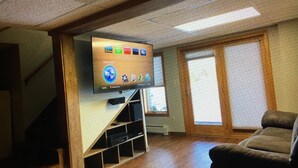 A living room with a flat-screen TV mounted on a wooden wall, a staircase, and a window with blinds. - Beautiful waterfront home nestled on 4acres on Indian Lake!
A perfect getaway!
 (Whiting)