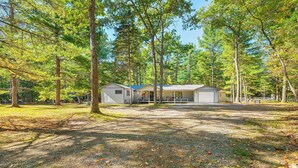 A cabin with a covered porch, surrounded by tall trees and a gravel driveway. - 2 Blocks to Boat Ramp: Higgins Lake House w/ Grill (Roscommon)