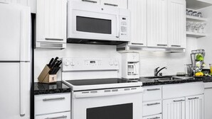 A kitchen with white cabinets, a microwave, a stove, and a coffee maker.