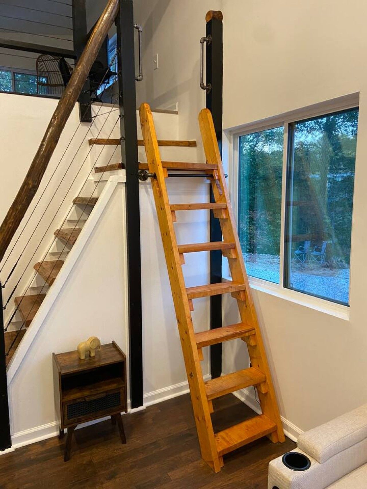 A wooden ladder leaning against a wall next to a staircase with a small table and a window.