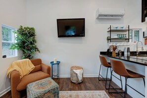 Een moderne woonkamer met een bank, een poef en een aan de muur bevestigde televisie.