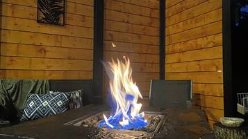 A fire feature with a metal grate, surrounded by wooden walls and a bench with patterned cushions.