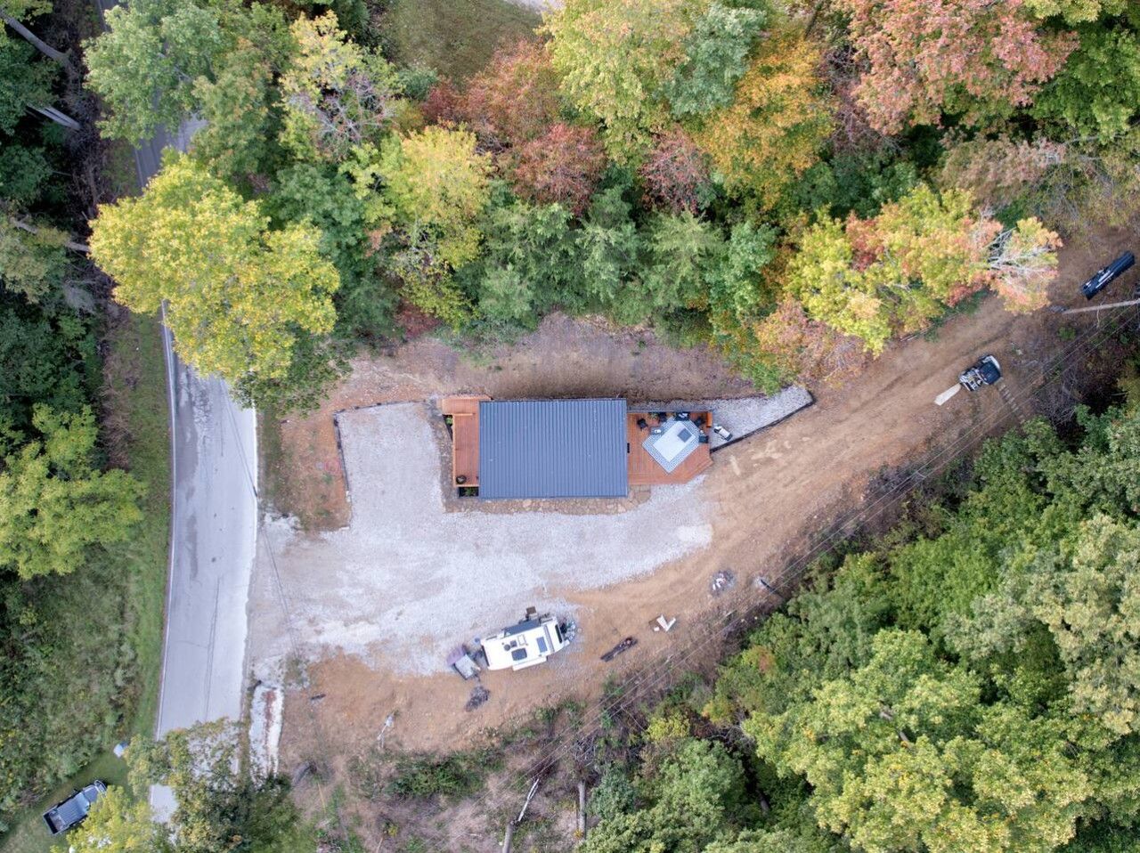 An aerial view of a property with a single building, a gravel driveway, and a parked vehicle.