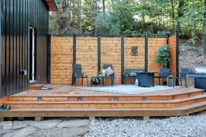 Een houten terras met buitenmeubels, een barbecue en een pad van stenen dat naar een gebouw leidt.