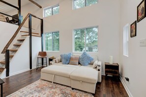 A spacious room with a large bed, a wooden staircase, and multiple windows.