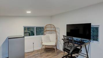 Habitación moderna con televisor de pantalla plana, una silla de madera, un escritorio con silla y un refrigerador.