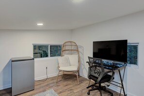 A modern room with a flat-screen TV, a wooden chair, a desk with a chair, and a refrigerator.