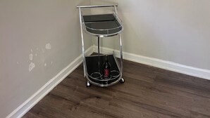A corner room with a wooden floor, a metal shelf unit with a bottle, and a window with blinds. - Charming 1-bedroom house rain Stone Mountain with WiFi access (Stone Mountain)