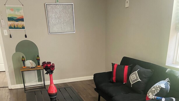 A living room with a black coffee table, a black sofa with decorative pillows, a red vase with flowers, and a small table with a decorative item and two candles. - Charming 1-bedroom house rain Stone Mountain with WiFi access (Stone Mountain)