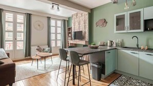 Une cuisine moderne dotée d’un îlot central, de tabourets de bar, d’une table à manger et d’une grande fenêtre agrémentée de rideaux.