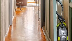 Un couloir avec un plancher en bois, un canapé et un aspirateur.