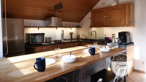 A modern kitchen with wooden cabinets, a stainless steel refrigerator, a coffee machine, and a wooden countertop with various kitchen items.