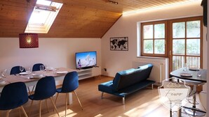 A cozy living room with a dining area, wooden ceiling, large windows, and a TV.