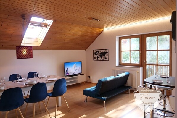 A cozy living room with a dining area, wooden ceiling, large windows, and a TV.