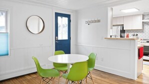 Ein Zimmer mit einem runden Tisch, vier grünen Stühlen, einer blauen Tür und einer Küchenzeile mit weißen Schränken und einem roten Handtuch.