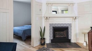 Una habitación con chimenea, una cama con ropa de cama azul, una planta en maceta y una mesita pequeña.