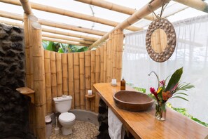 Ein Badezimmer mit Bambusstruktur, einer Steinwand, einer Toilette, einem Waschbecken und einem Spiegel mit Muscheln.