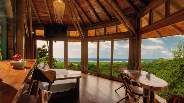 A wooden interior with a dining area, a bed, and large windows overlooking a landscape. - Cabañas Cochapunko I Espectacular vista 360 (Salango)