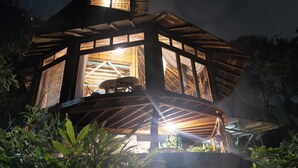 A wooden cabin with a large central window and a smaller window on the side, surrounded by lush greenery. - Cabañas Cochapunko I Espectacular vista 360 (Salango)