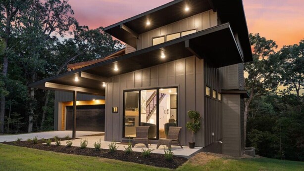 A modern two-story house with a large sliding glass door entrance, a covered patio area, and a well-maintained garden. - Elevated Chalet with Hot Tub Scenic Views & Trail Access (Bella Vista)
