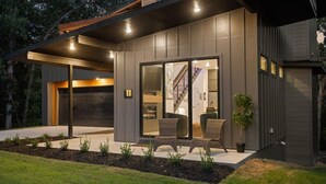 A modern house with a covered patio, large sliding glass doors, and a staircase leading to the interior. - Elevated Chalet with Hot Tub Scenic Views & Trail Access (Bella Vista)