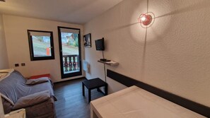 A room with a bed, a small table, a TV on the wall, and a door leading to an outdoor area.