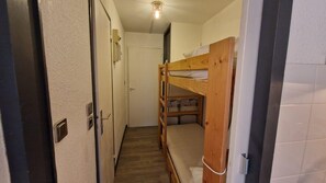 A narrow hallway with a bunk bed on the right, a door on the left, and a light fixture on the ceiling.