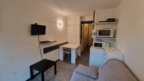 Una habitación funcional con cama, escritorio, televisor, microondas y pequeña cocina.