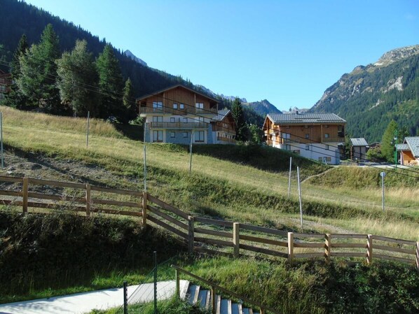 A wooden chalet with a balcony, set against a mountainous backdrop.
