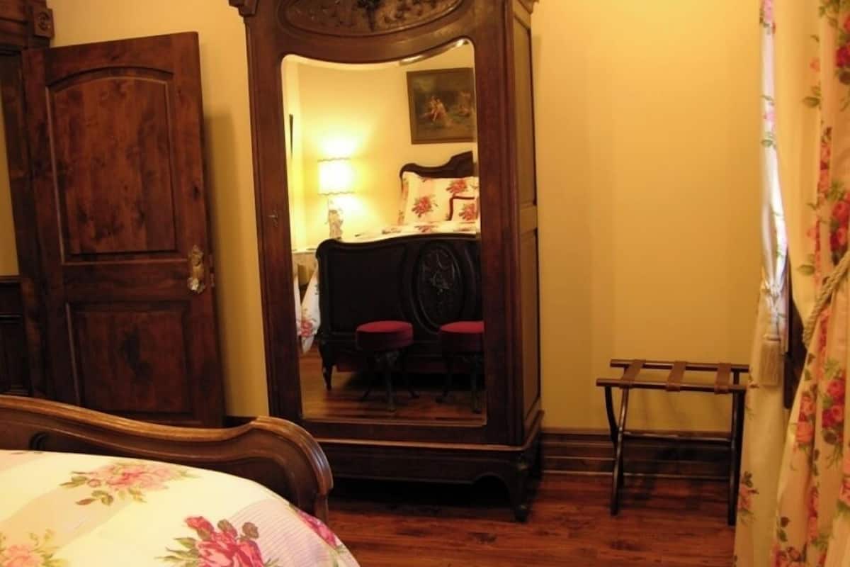 Une chambre avec une armoire en bois, un lit avec une literie à motifs floraux, une chaise et une petite table.