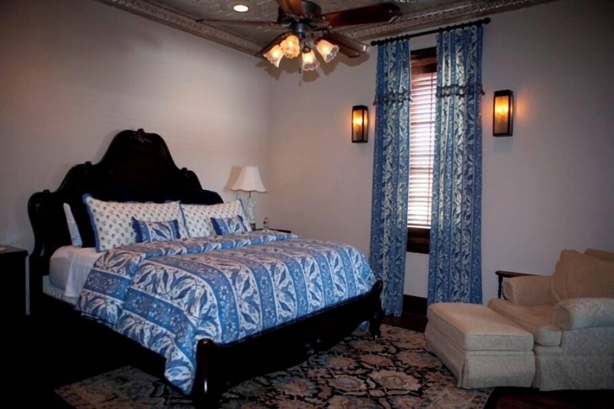 Une chambre avec un grand lit, un ventilateur de plafond, des rideaux à motifs et un canapé.