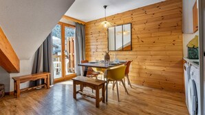 A dining area with a wooden table, chairs, and a bench. There is a window with curtains, a wooden wall, and a ceiling with a sloped design. - 40m from ski slopes, 3rd floor, fitness, swimming pool, sauna, balcony, tv, ski locker, 39m² (Les Orres)