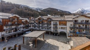 A ski resort with wooden buildings, outdoor seating, and a mountainous backdrop. - 40m from ski slopes, 3rd floor, fitness, swimming pool, sauna, balcony, tv, ski locker, 39m² (Les Orres)