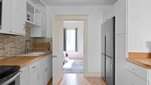 Une cuisine étroite avec des meubles blancs, un plan de travail en bois et un réfrigérateur en acier inoxydable.