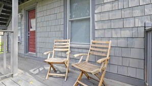 Deux chaises en bois sur une véranda en bois, avec un revêtement extérieur gris et une porte rouge.