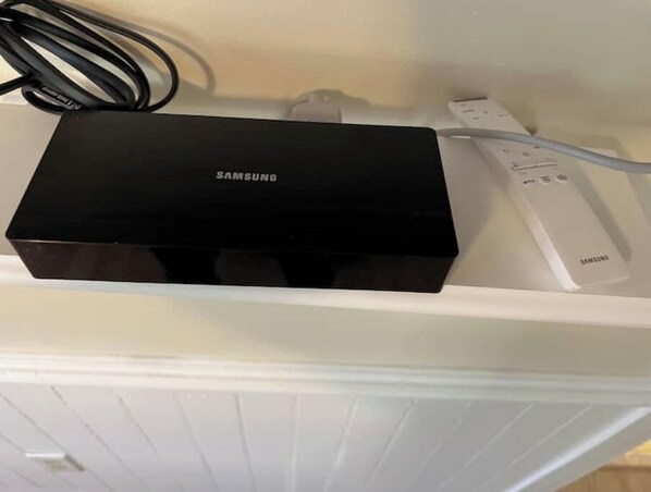 Una caja de Samsung y un control remoto blanco sobre un estante blanco.
