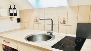 Una cocina con un lavamanos de acero inoxidable, una placa de inducción negra y una encimera de madera.