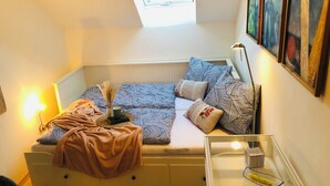 Un dormitorio tipo loft acogedor con techo inclinado, cama con ropa de cama estampada, lámpara de noche y obras de arte en las paredes.