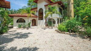 A two-story house with a gravel driveway, surrounded by lush greenery and palm trees. - Jungle Villa w/ Lush Gardens walk 2 Pelada Beach (Nosara)