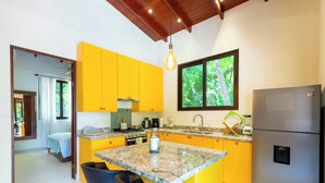 A modern kitchen with yellow cabinets, a granite countertop, and a stainless steel refrigerator. - Jungle Villa w/ Lush Gardens walk 2 Pelada Beach (Nosara)