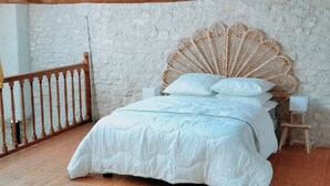 Une chambre avec un plafond en bois, un lit avec une literie blanche, un tapis rond et une table de chevet en bois.
