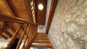 Un escalier en bois, avec un mur en pierre d’un côté et un luminaire au plafond.