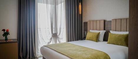 A hotel room with a large bed, a desk, and a window with curtains.